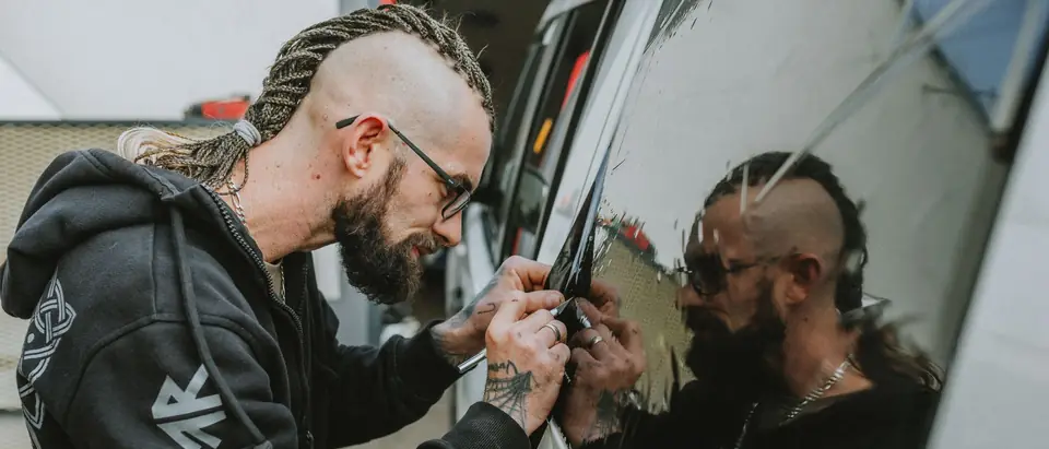 An installer working a squeegee along a car's side window