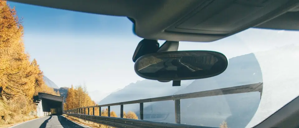 A windshield seen from the driver's seat, the mirror and the road beyond it
