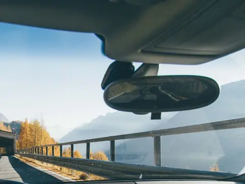 A windshield seen from the driver's seat, the mirror and the road beyond it