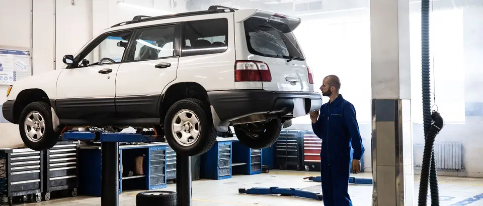 A technician in blue coveralls beside a raised SUV in a clean, bright shop
