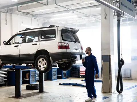 A technician in blue coveralls beside a raised SUV in a clean, bright shop