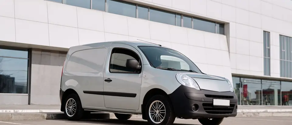 A small white service van parked beside a modern building